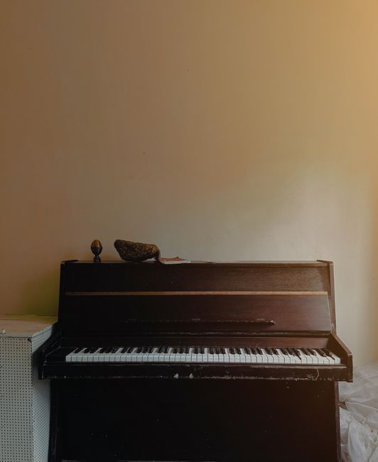 Close-up image of a section of a piano keyboard showing white keys labeled with small pieces of paper with handwritten musical note names: C, D, E, F, G, A, B, and an additional label with the number 